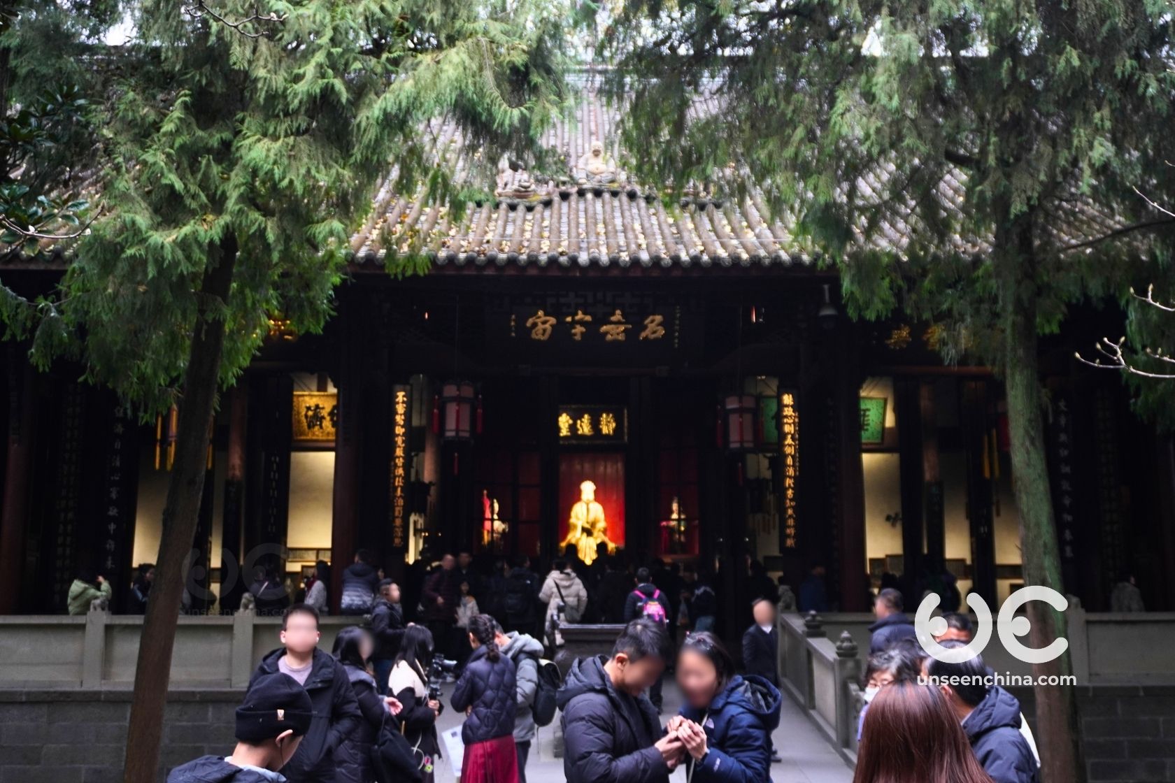 A crowd of visitors inside the traditional timber-framed hall, viewing the prominent seated statue of the strategist Kongming at the Wuhou Shrine.