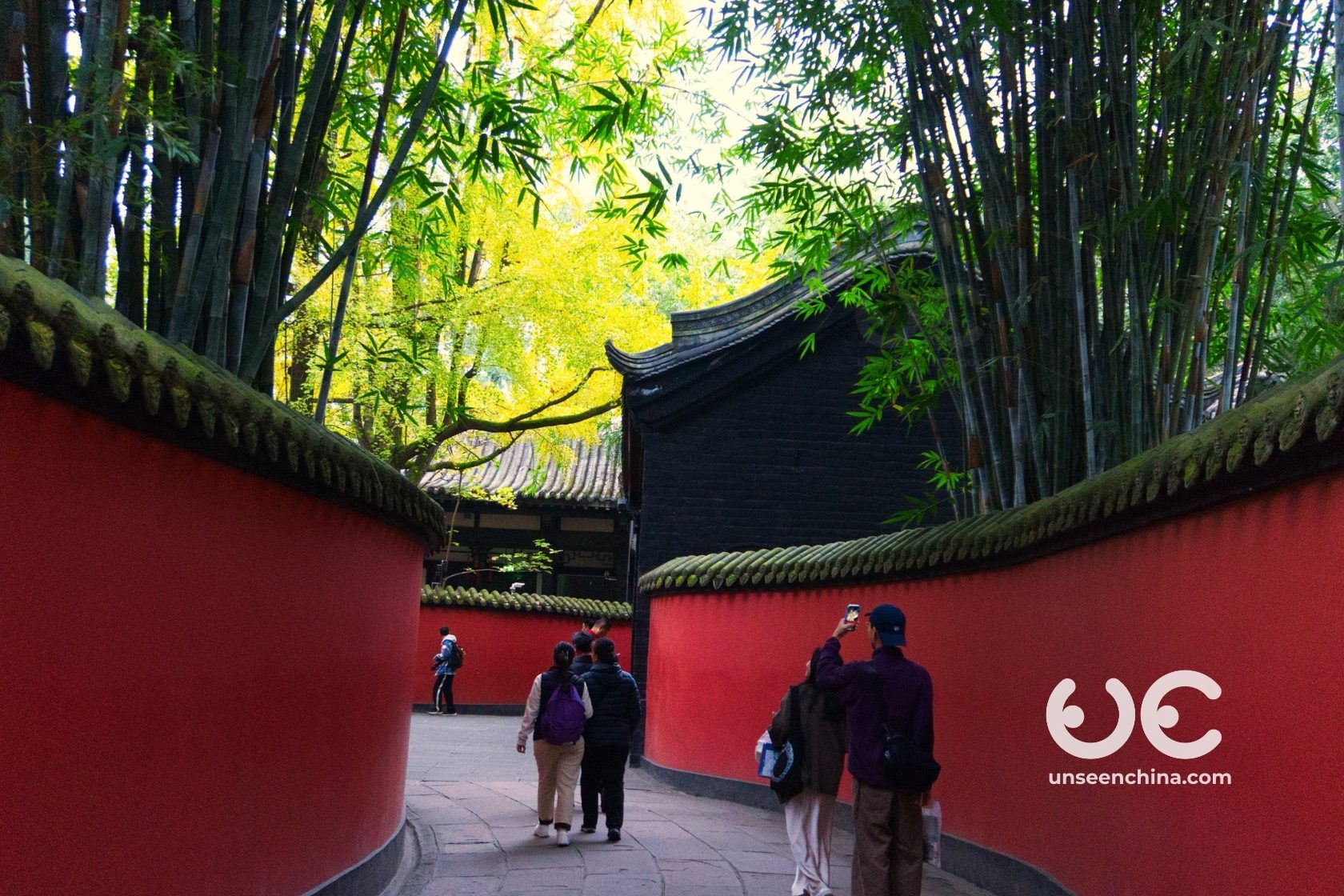 People taking photos in front of the iconic curving red wall at the Wuhou Shrine with bamboo trees.