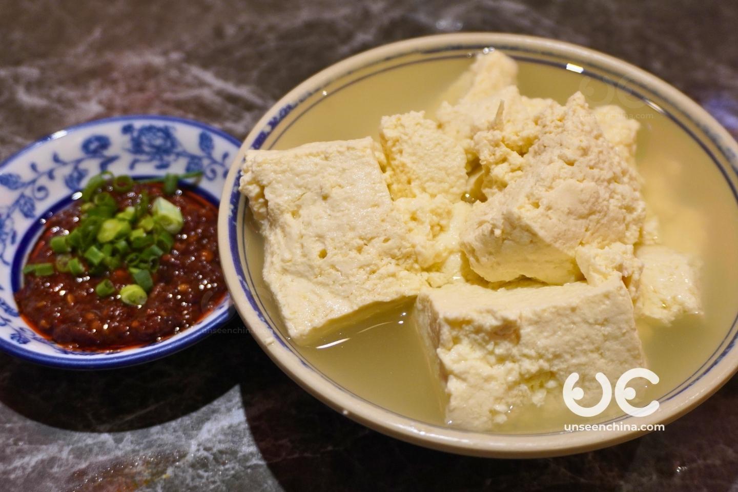 A bowl of douhua tofu served with Sichuan chili sauce in a small dipping bowl