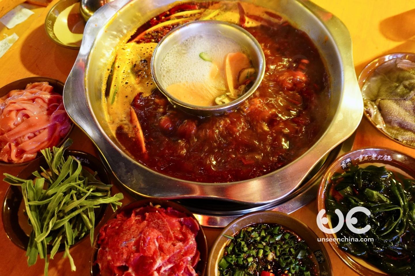 Sichuan hotpot with a split pot, spicy mala broth on the outer ring and clear broth in the center, surrounded by meats and vegetables