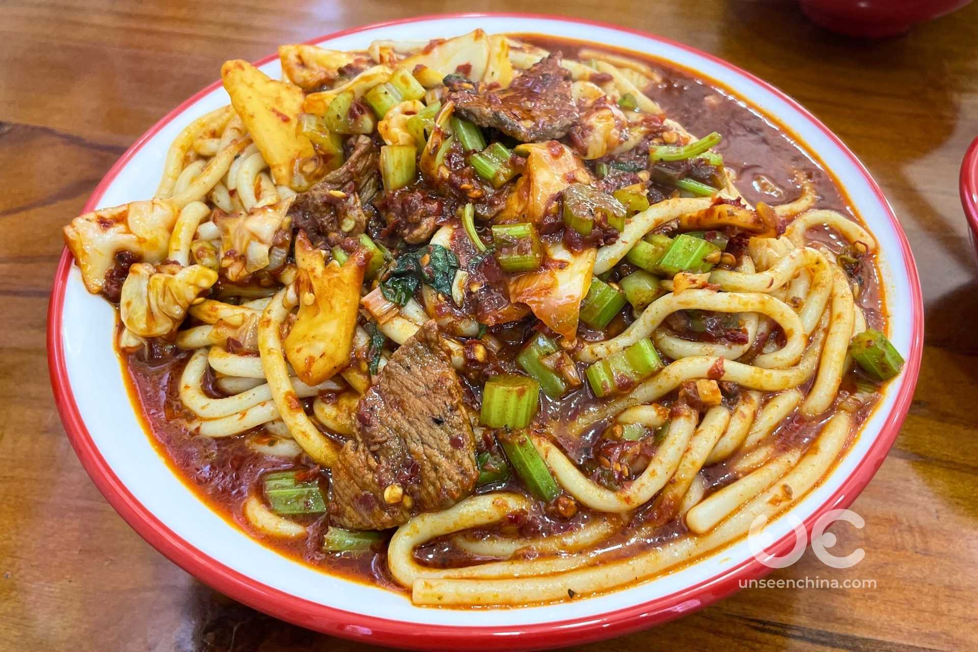 Xinjiang fried rice noodles served in a dish with pieces of meat, vegetables, and spicy red sauce.